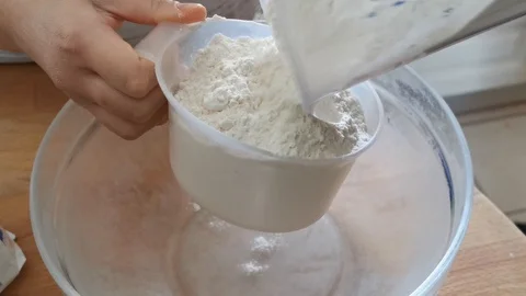 Closeup view of a young lady is measuring baking flour with measuring cup Stock Footage 128457082