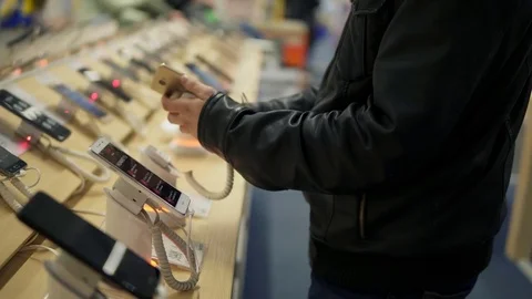 Closeup view of a young man's hands choosing a new mobile phone in a shop. He is 스톡 동영상 83751017