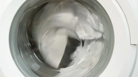 Closeup of washing machine door with spinning white laundry Stock Footage
