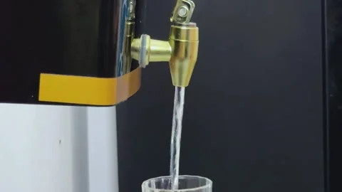 Closeup of water being poured from a brass tap into a clear glass held by a.. Vidéo 340053146