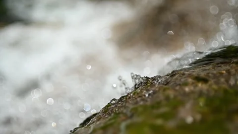 Closeup of water running over a rock in front of a waterfall (slow motion) Video stock 219636351