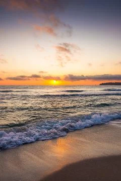 Closeup of wave rolling on sandy shore at golden sunrise Stock Photos