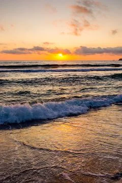 Closeup of wave rolling on sandy shore at golden sunrise Stock Photos