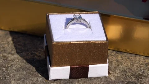 Closeup on a wedding ring, a golden present box and a red rose on a stony Stock-Footage 104082002