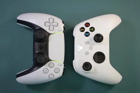 Closeup of a white Xbox controller and white ps5 controller on a blue background Stock Photos