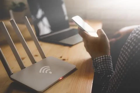 Closeup of a wireless router and a man using smartphone on living room at h.. Stock Photos