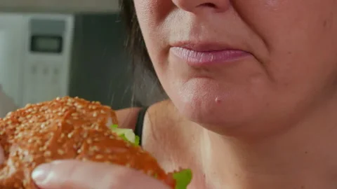 Closeup of woman talking while eating tasty burger in kitchen at home Stock Footage 290188337