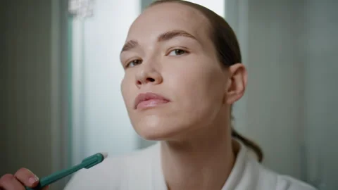 Closeup woman using toothbrush in bathroom setting. Focused girl looking camera Stock Footage 278466936