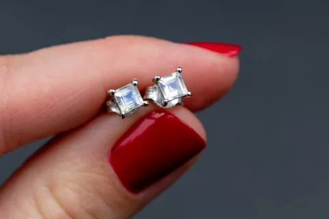 Closeup of a woman's hand with red manicure holding a diamond earrings Stock Photos