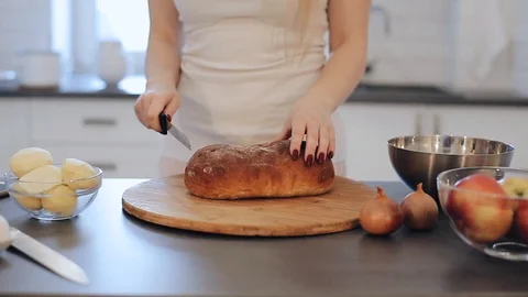 Closeup of womans hands cutting bread. Cooking in kitchen. Caucasian girl in Видео 103308371
