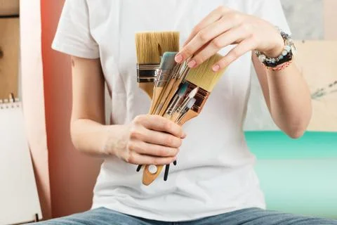 Closeup of woman's hands holding and picking various paint brushes, selective Stock Photos