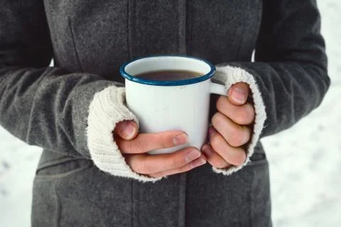 Closeup of woman's hands holding white enamel cup with hot drink outdoors, se Stock Photos