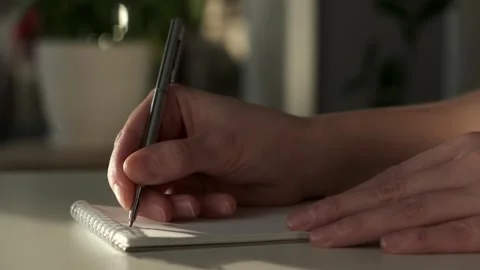 Closeup of woman's hands journaling in a white notebook on a white table at home Stock Footage 260759429