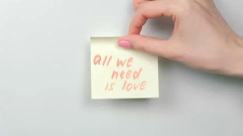 Closeup woman's hands stick yellow sticker paper sheets with words all we need Stock Footage 87807780
