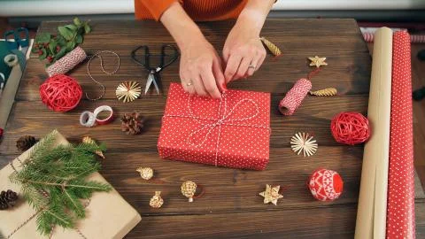 Closeup of woman's hands while wrapping Christmas present, on wood table Stock Photos