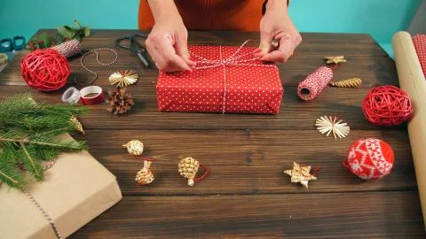 Closeup of woman's hands while wrapping Christmas present, on wood table Stock Photos