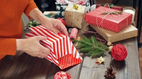 Closeup of woman's hands while wrapping Christmas present, on wood table Stock Photos