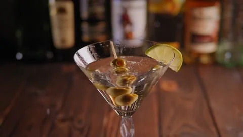 Closeup of wooden toothpick with three green olives falling into a Martini glass Stock Footage