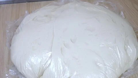 Closeup of yeast dough covered with plastic wrap on a professional kitchen table Stock Footage 318139315