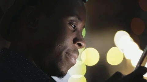 Closeup of young african man looking down to smartphone in city at night Stock Footage