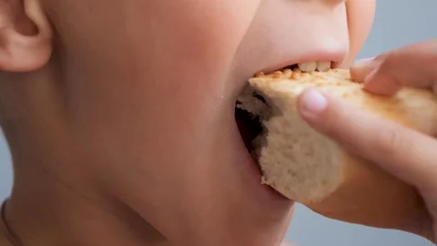 A closeup of a young boy excitedly biting into a piece of fresh white bread Stockbeeldmateriaal 288040023
