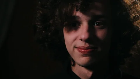 Closeup of young cute man touching his long curly hair in the dark room Stock Footage 99050372