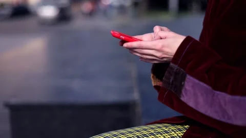 Closeup of young female hands using red smartphone on sunny street chatting 스톡 동영상 131016565