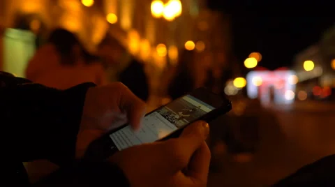Closeup of young man hands scrolling internet on phone. Night illuminated city Stock Footage 69070328