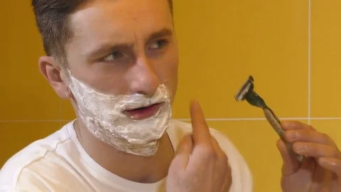 Closeup of young man shaving in the mirror Stock Footage 71777831