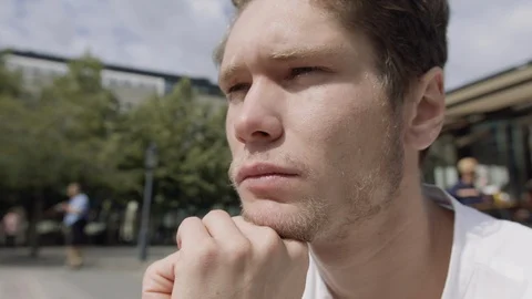 Closeup of a young man sitting down and thinking in a city square. 스톡 동영상 115987716