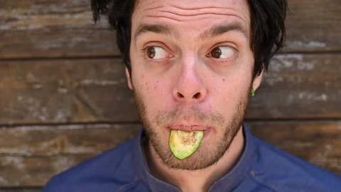 Closeup of young man using a slice of  zucchini as a tongue making funny faces Stock Footage 107535494