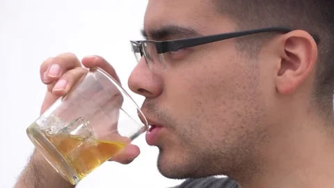 Closeup of a young white man with glasses drinking wiskey with ice in a glass Vidéo 155807864