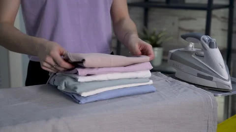 Closeup young woman's hands stacking ironed and folded clothes on ironing board Stock Footage 267952110