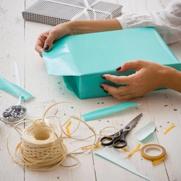 Closeup of a young woman's hands wrapping a festive gift in a turquoise paper Stock Photos