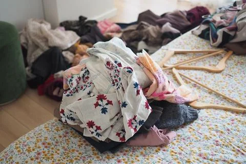 Clothes are piled on a bed in a messy bedroom Stockfoto's