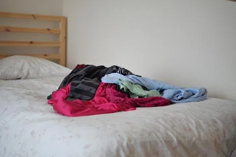 Clothes are piled on a bed in a simple room 스톡 사진