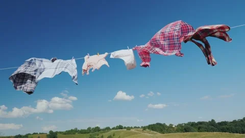 Clothes drying on clothesline blowing in wind against blue sky and green hill Stock Footage 334644055
