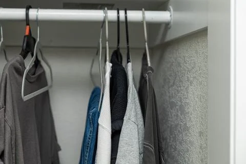 Clothes hanging inside open wardrobe, featuring shirts, jeans, jackets, hangers Stock Photos