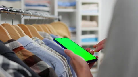 Clothes, Shop worker In process Looks at phone screen Online selection of cl Stock Footage 234407032