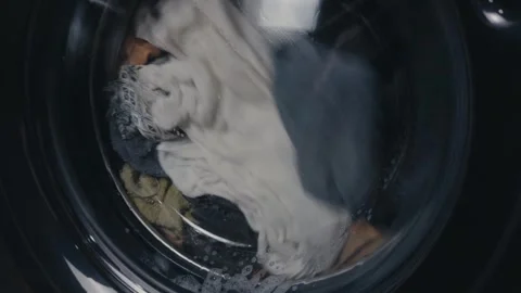 Clothes spinning inside a modern washing machine drum, water and suds creating Stock Footage 344911649