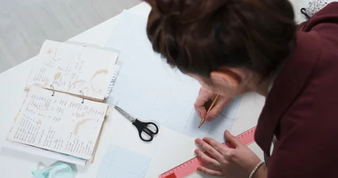 Clothing designer is working on studio table, drawing scheme outline of clothes Stock Footage 153010673