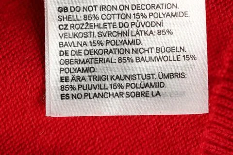 Clothing label in different languages on red garment, closeup Stock Photos