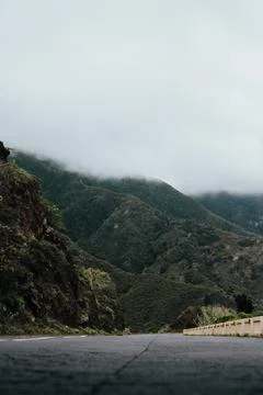 Cloud-covered mountains along a winding road in a tranquil landscape Stock Photos