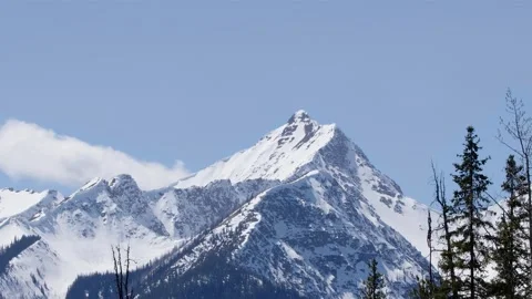 Cloud drifts slowly over rocky mountain peak with snow summit, nature Stockbeeldmateriaal 335126079