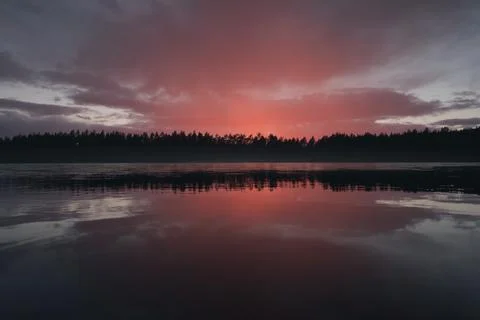 A cloud illuminated by the setting sun over a picturesque forest lake Foto stock