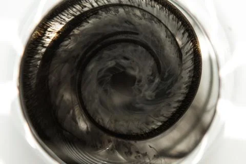 A cloud of ink in a transparent glass cup with clear water amid rays of light Stock Photos