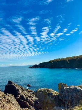 Cloud patterns reflect over the ocean near rocky coast during bright daylig.. Photos