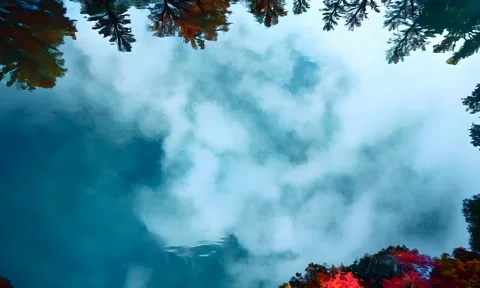 Cloud reflections on a serene lake surrounded by vibrant autumn foliage Stock Footage 298824414