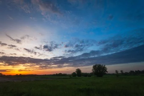 Cloud in the sky after sunset over a green meadow, May evening Stock Photos