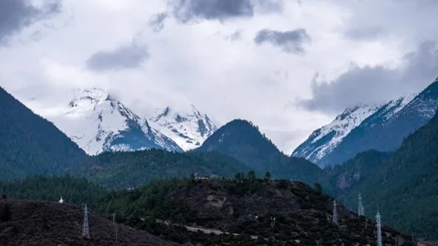 Cloud veiled snowy peak beyond a forested Tibetan hillside Vidéo 345882622